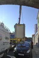 [Crane on truck unloading a large box]